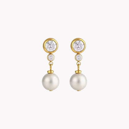 A pair of gold drop earrings featuring a round clear crystal, a small clear accent stone, and a dangling white pearl, shown against a plain light gray background.