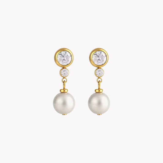 A pair of gold drop earrings featuring a round clear crystal, a small clear accent stone, and a dangling white pearl, shown against a plain light gray background.