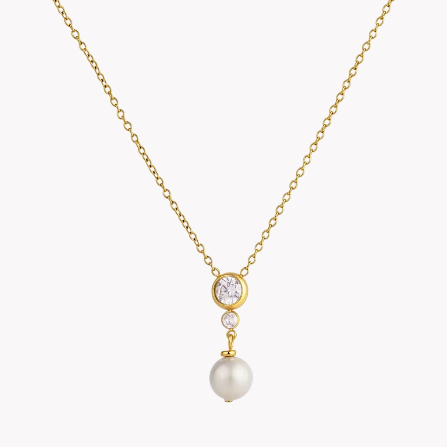 A delicate gold chain necklace featuring a pendant with a round clear stone, a small clear stone, and a dangling white pearl, set against a light gray background.