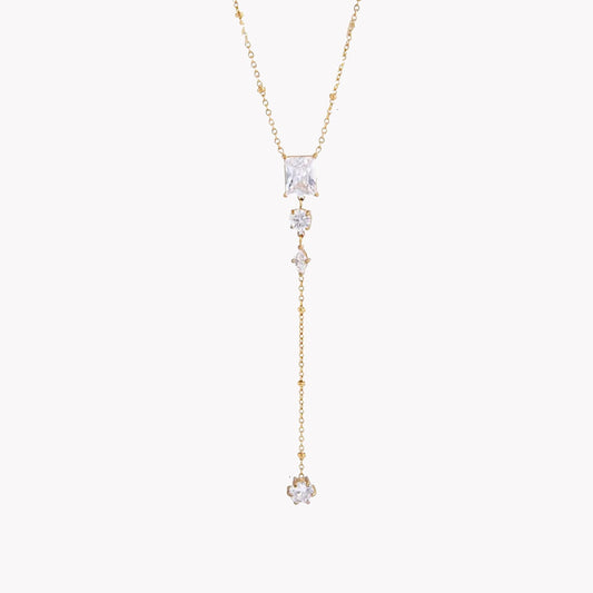 gold necklace featuring clear gemstones of different shapes pictured on a light grey background