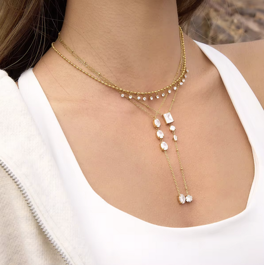 gold necklace featuring clear gemstones of different shapes pictured being worn