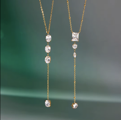 gold necklace featuring clear gemstones of different shapes pictured hanging with a blue background