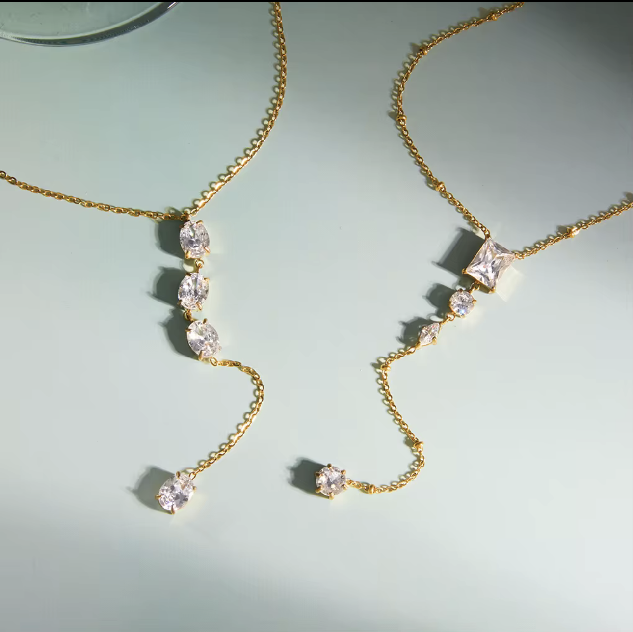 gold necklace featuring clear gemstones of different shapes pictured on a light blue background