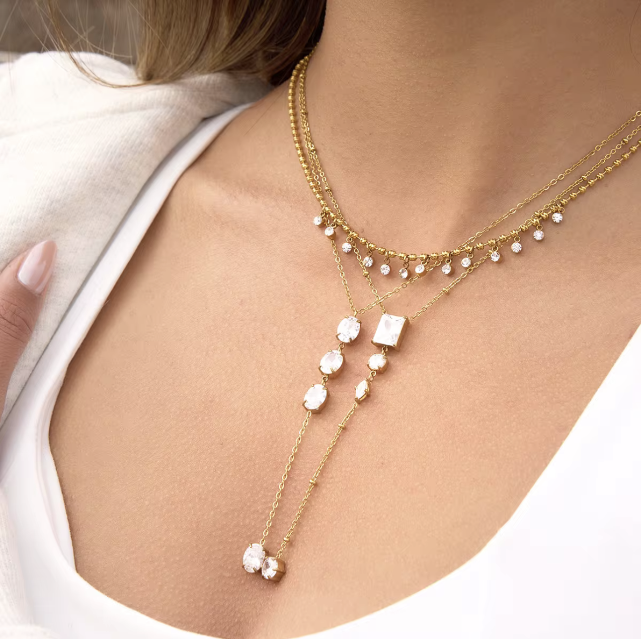 gold necklace featuring clear gemstones of different shapes pictured being worn