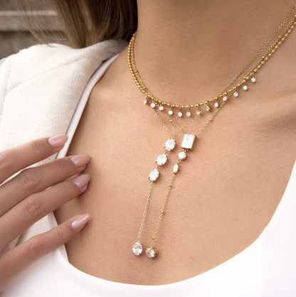 gold necklace featuring clear gemstones of different shapes pictured being worn