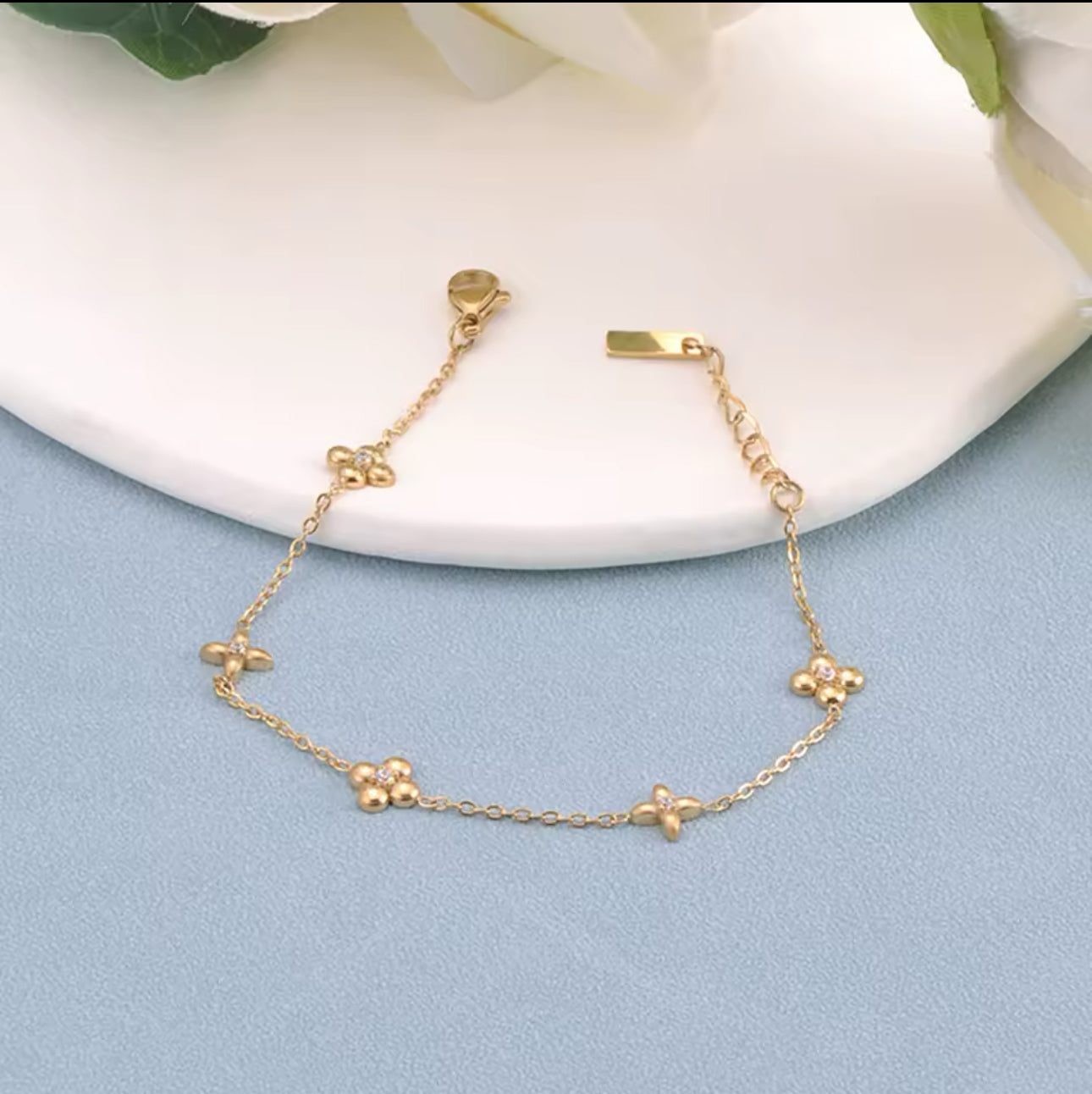 gold bracelet with flower detail on a light blue and white background