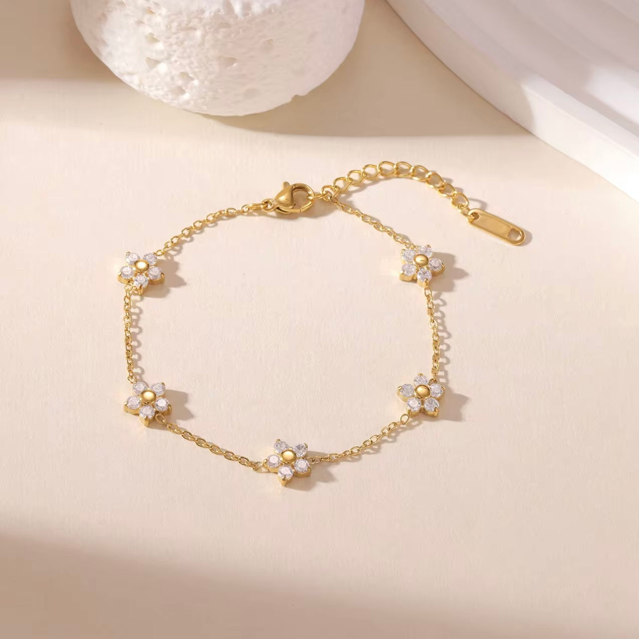 Gold bracelet with clear gemstone floral design on a biege background