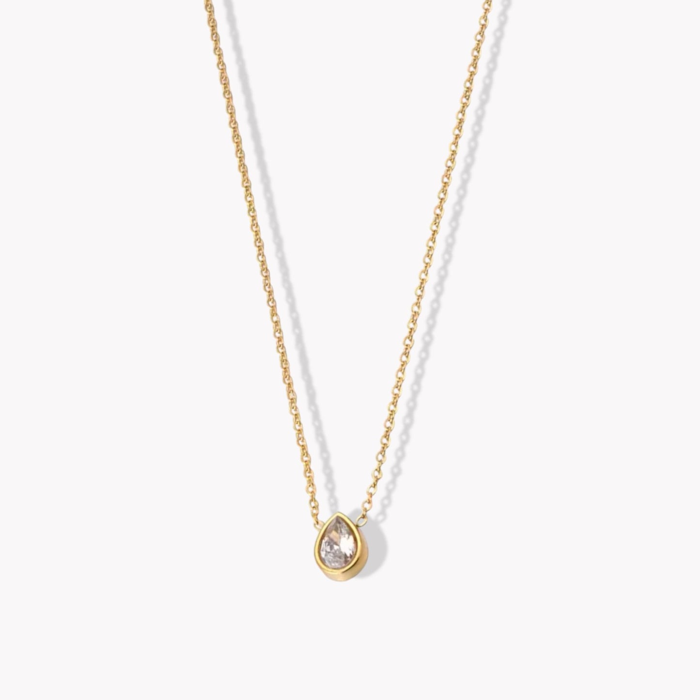 A gold-colored pendant necklace with a pear shaped zircon gemstone on a fine chain, displayed against a white background.