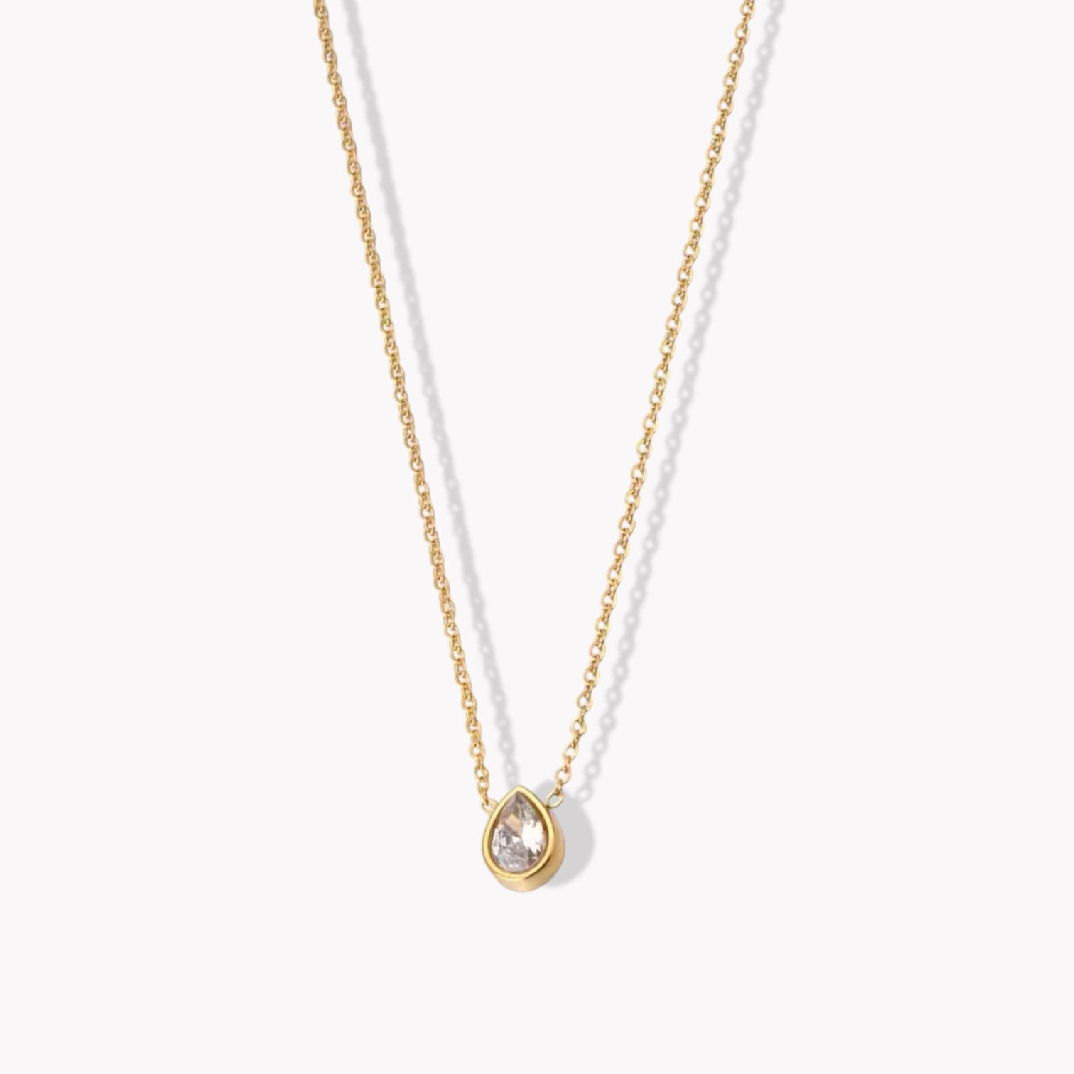 A gold-colored pendant necklace with a pear shaped zircon gemstone on a fine chain, displayed against a white background.