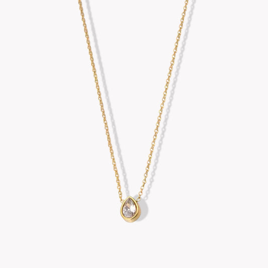 A gold-colored pendant necklace with a pear shaped zircon gemstone on a fine chain, displayed against a white background.