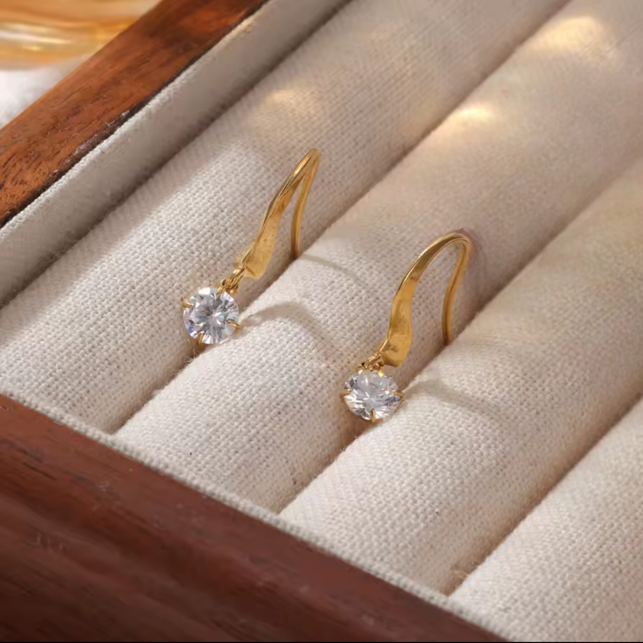 Gold earrings with clear gemstones on a beige jewelry box