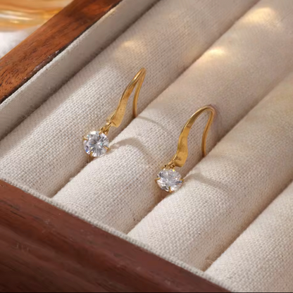 Gold earrings with clear gemstones on a beige jewelry box