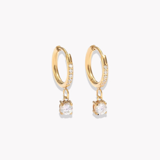 Gold hoop earrings with diamonds on the hoop and a round shaped drop pendant on a white background