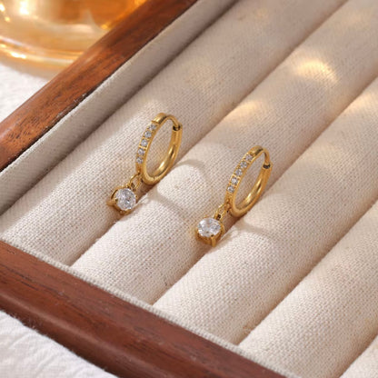 Gold hoop earrings with diamonds on the hoop and a round shaped drop pendant on a biege background