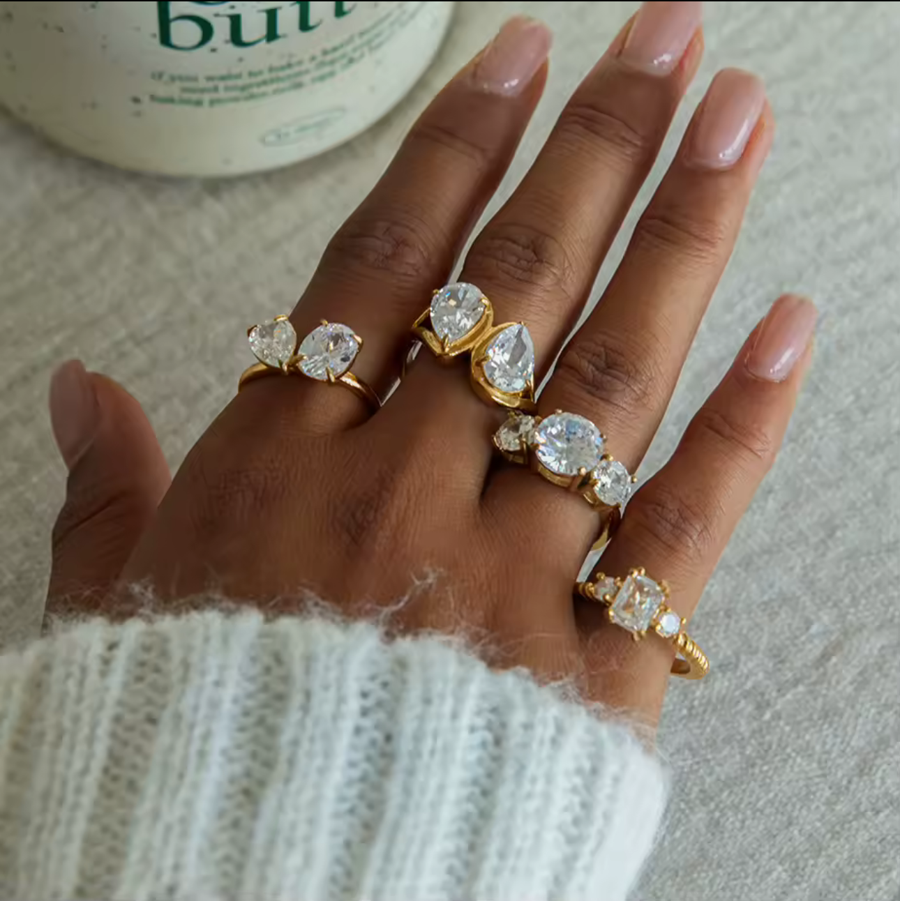 Hand wearing multiple gold rings with diamond accents on a neutral background