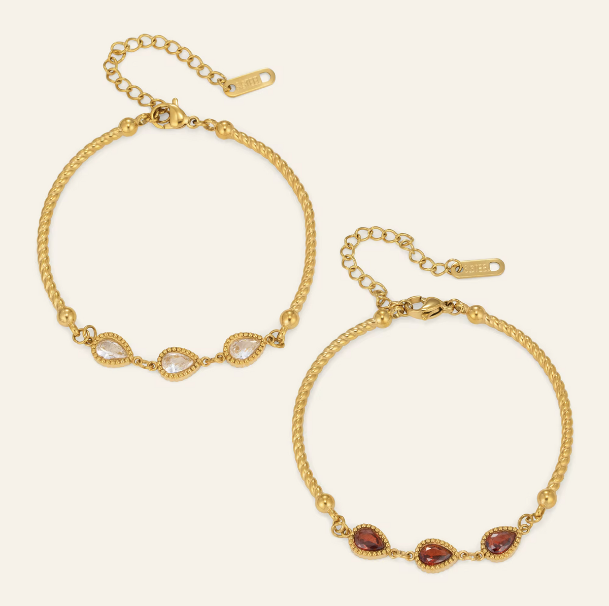 Two gold chain bracelets with oval and marquise-cut stones, displayed on a light cream background. One bracelet features a clear oval stone, and the other features three reddish-brown marquise stones.