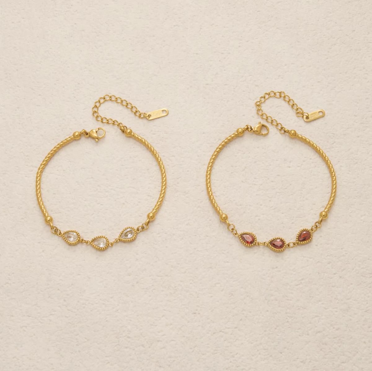 Two gold-toned delicate bracelets displayed on a textured off-white background. The left bracelet features a twisted rope design with a central infinity loop set with small clear stones.