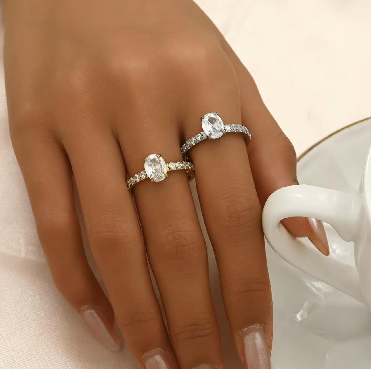 Silver ring with oval gemstone and further gemstones along the band of the ring, pictured on a hand