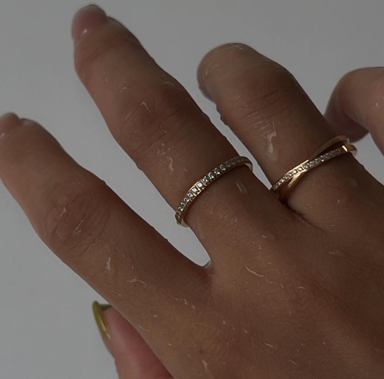 Hand wearing two gold rings with diamond accents on a plain background