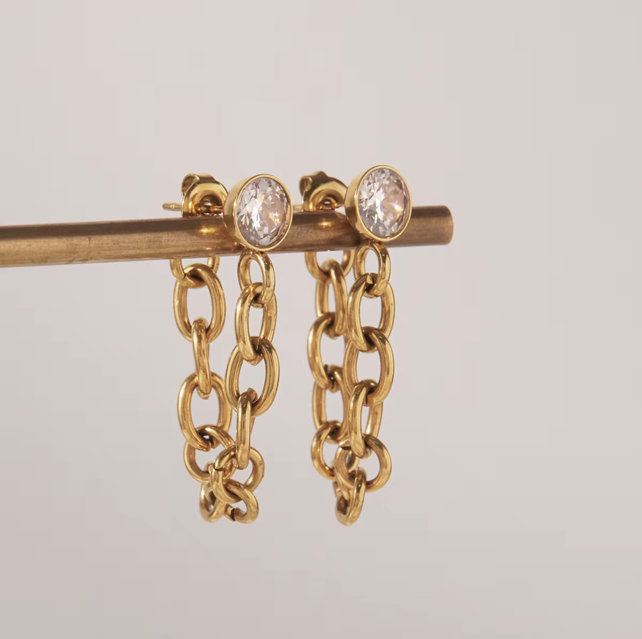 Gold Earrings with long chain detail shown hanging on a small pole with a grey background