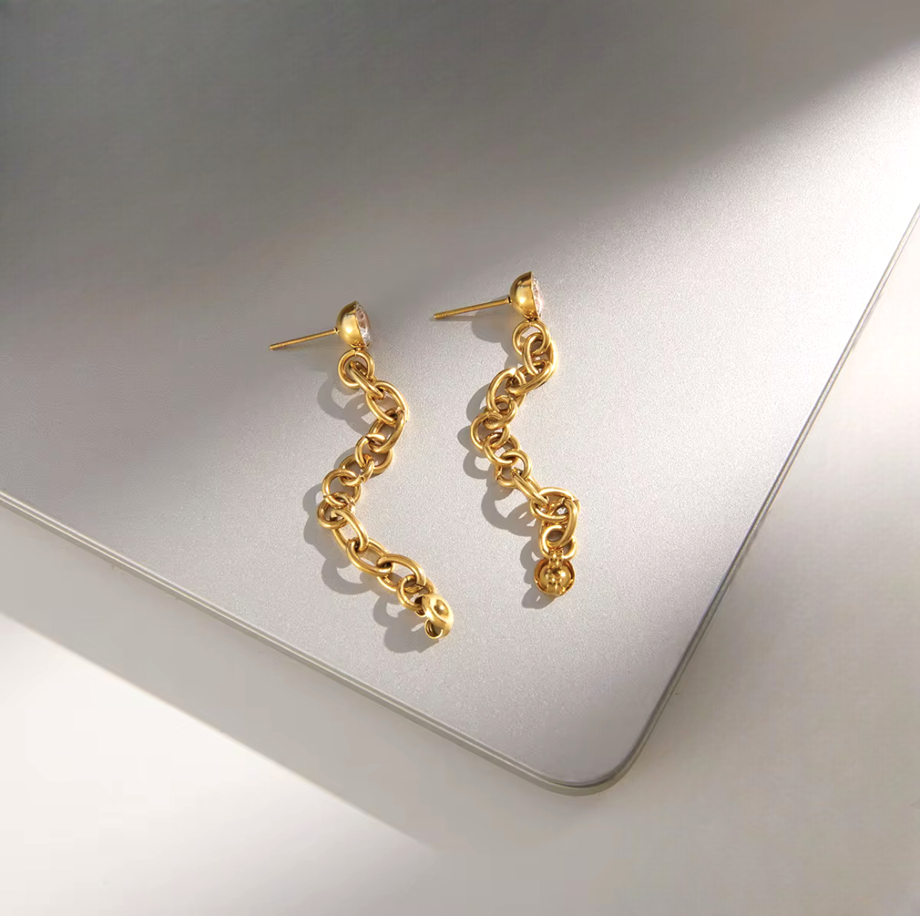 Gold Earrings with long chain detail laid on a grey background