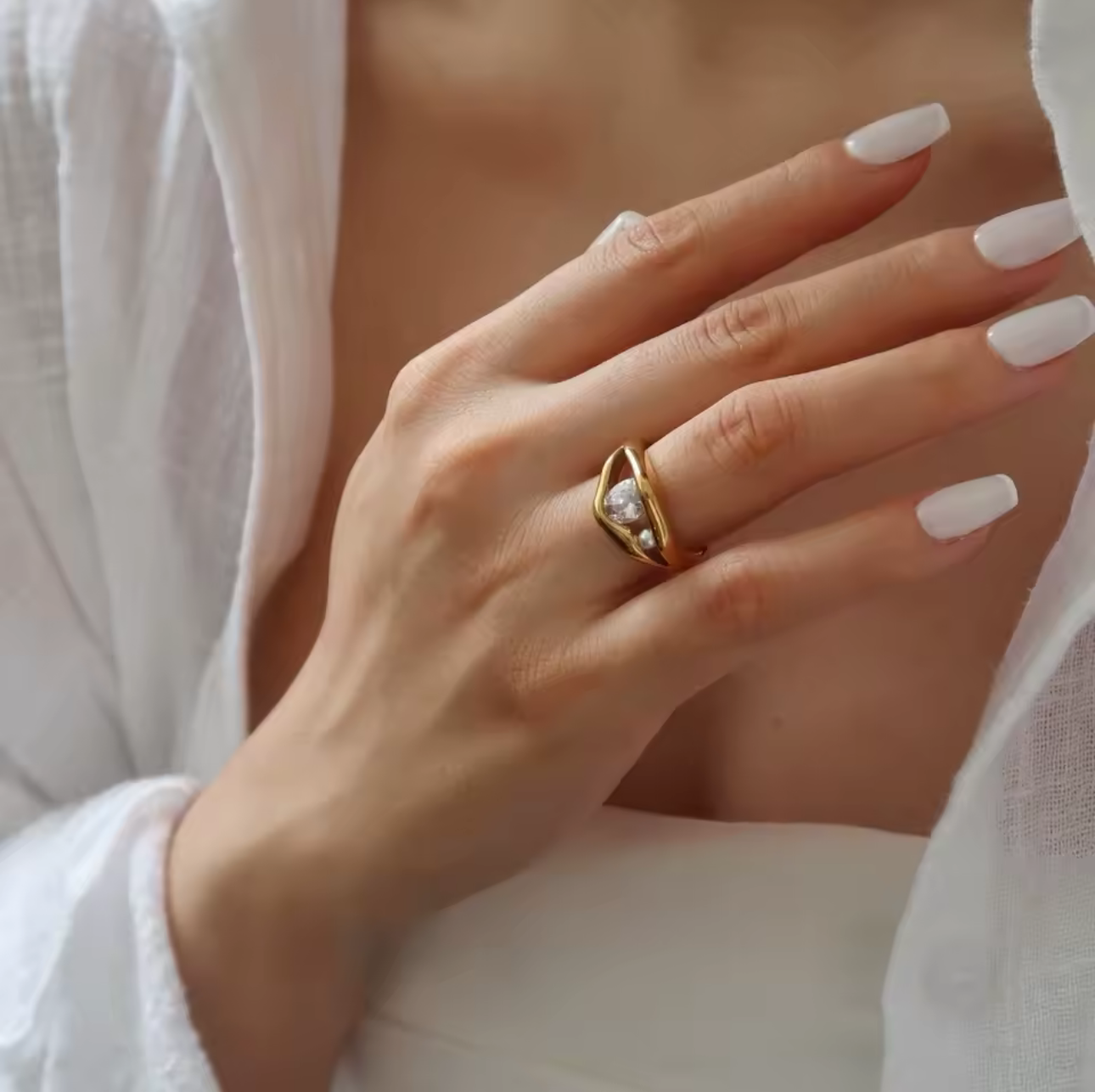 Close-up of a hand wearing a gold ring with a diamond, against a neutral background.