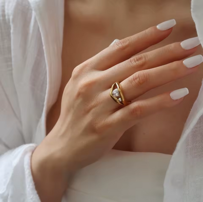 Close-up of a hand wearing a gold ring with a diamond, against a neutral background.