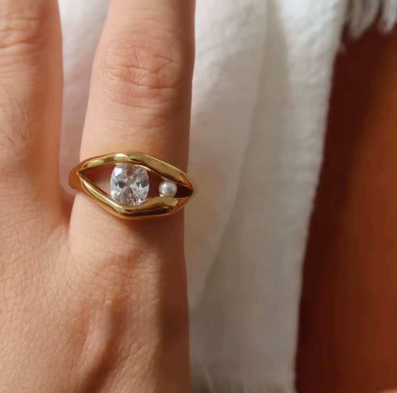 Gold ring with a diamond on a person's finger against a neutral background