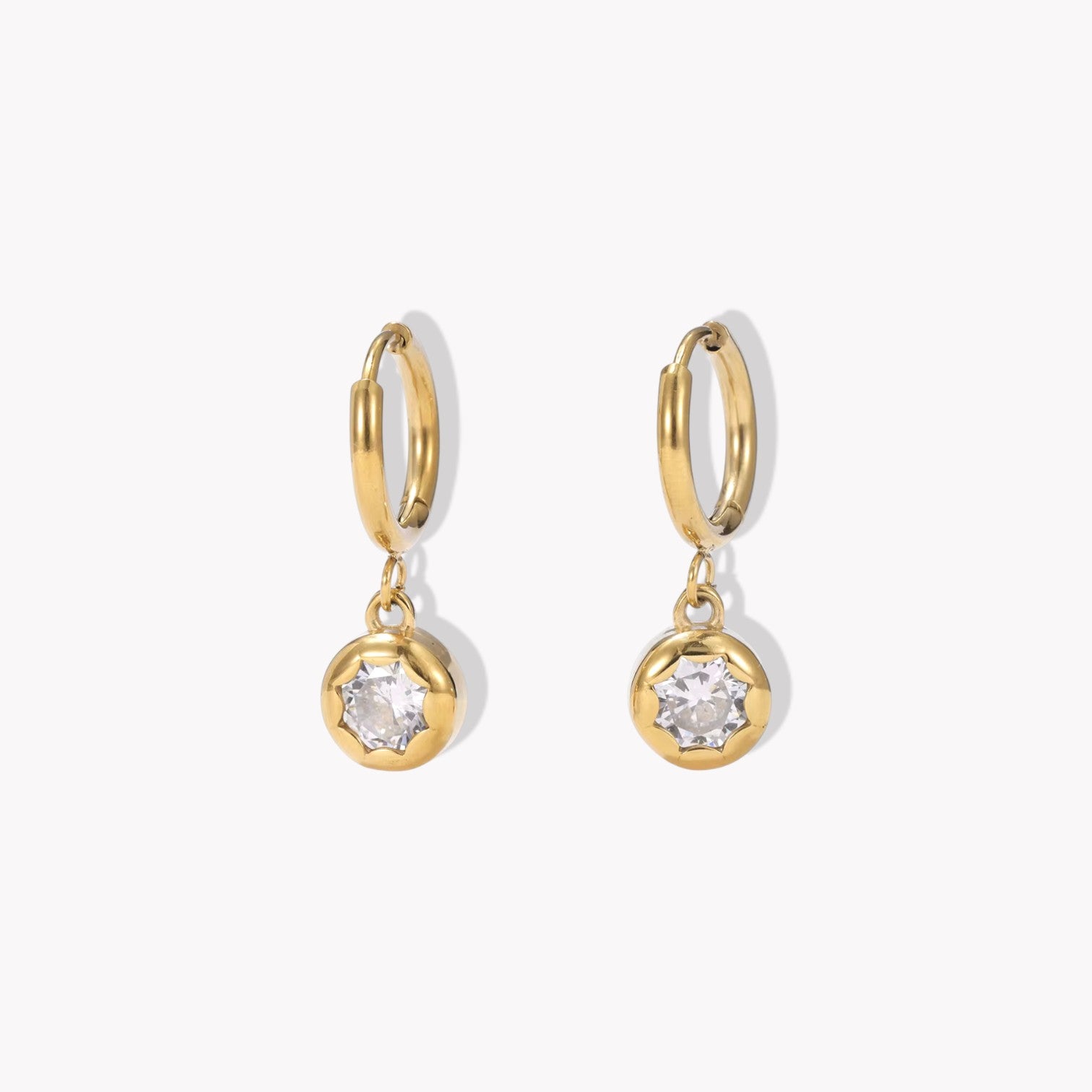 gold hooped earrings with bezel set drop gemstone pictured on a light beige background