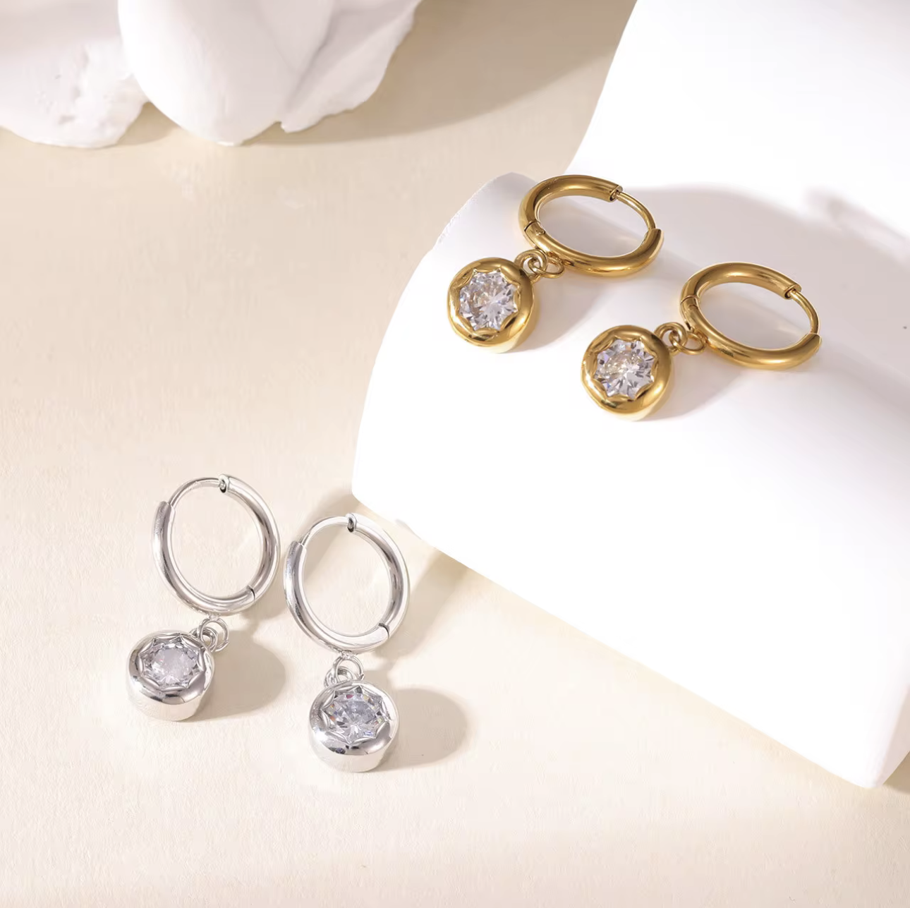 gold and silver hooped earrings with bezel set drop gemstone pictured on a light beige background