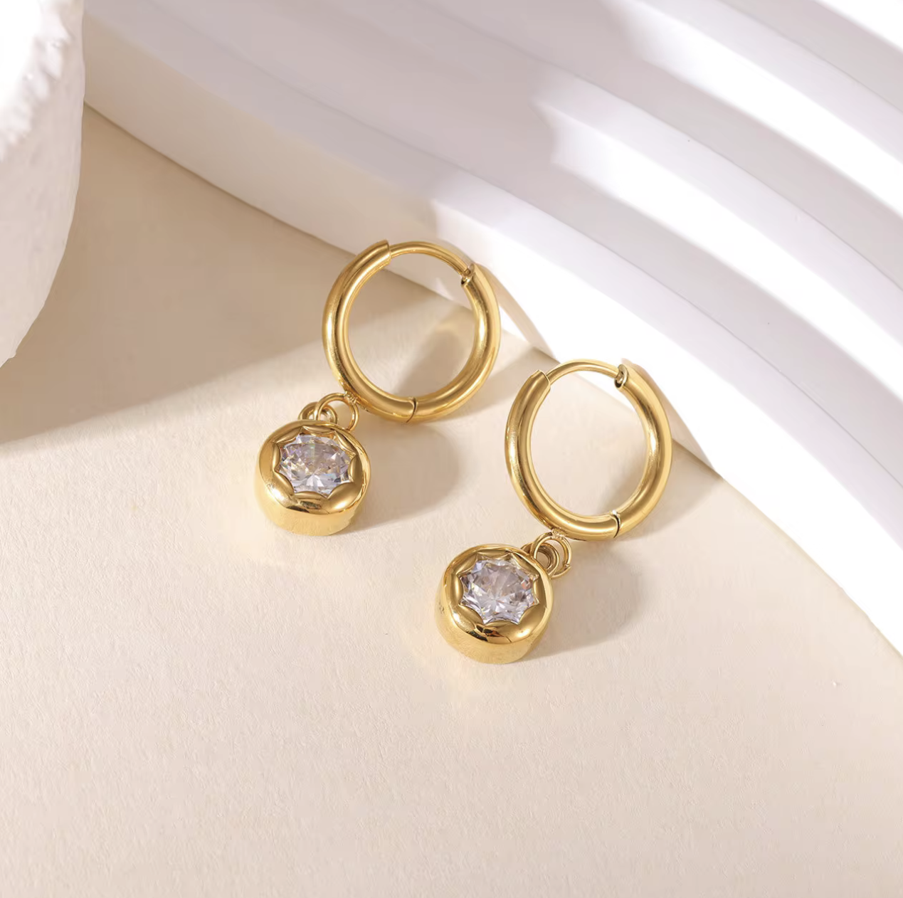 gold hooped earrings with bezel set drop gemstone pictured on a light beige background