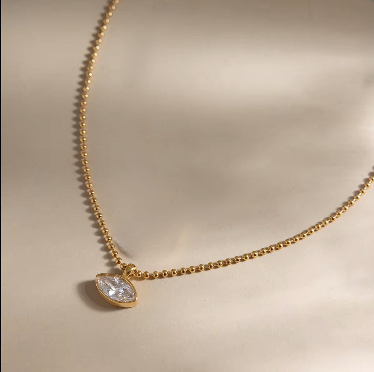 Gold necklace with a teardrop-shaped diamond pendant on a beige background