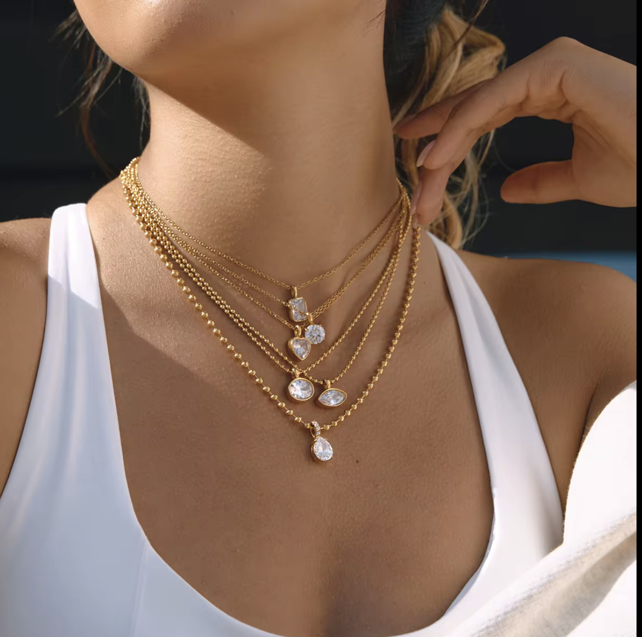 Close-up of a woman wearing multiple gold necklaces with a white top.