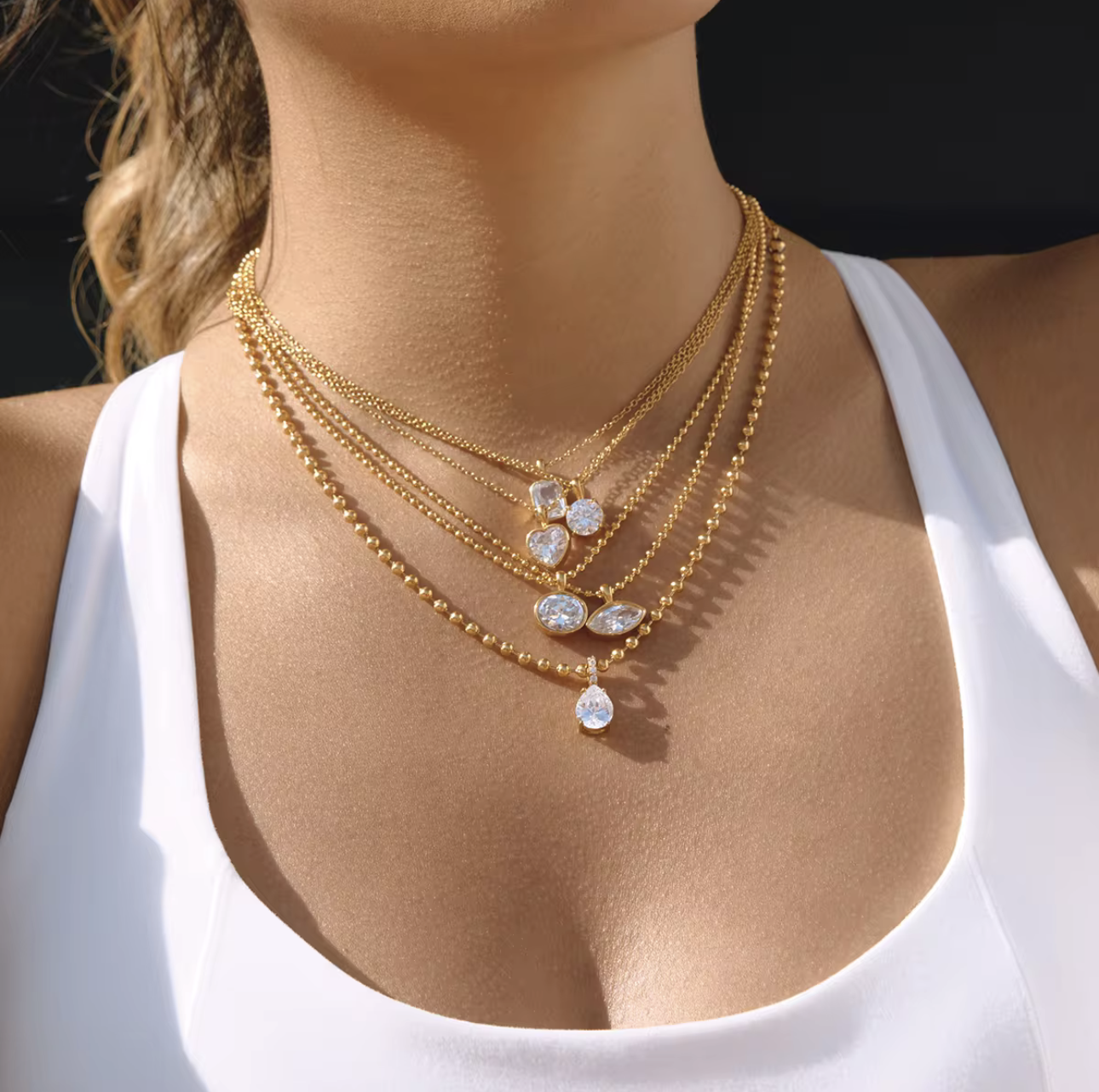 Gold necklace with heart-shaped pendants on a model wearing a white top.