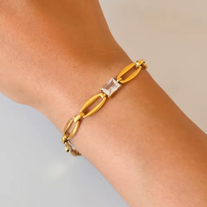 Gold bracelet with a clear gemstone on a wrist against a neutral background