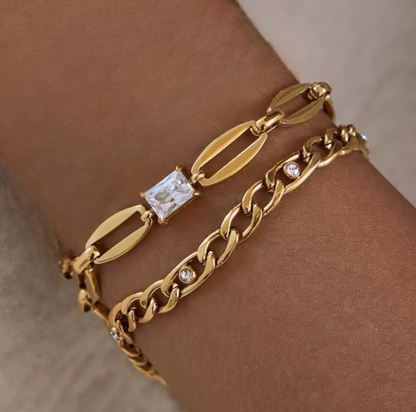 Gold bracelets with diamond accents on a wrist against a neutral background