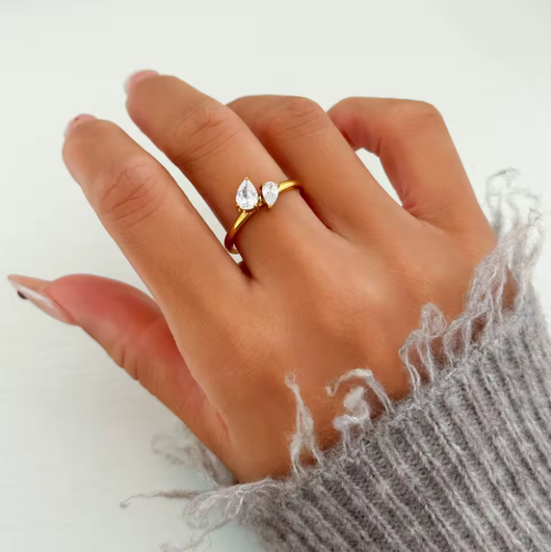 Hand wearing a gold ring with three clear stones on a white background