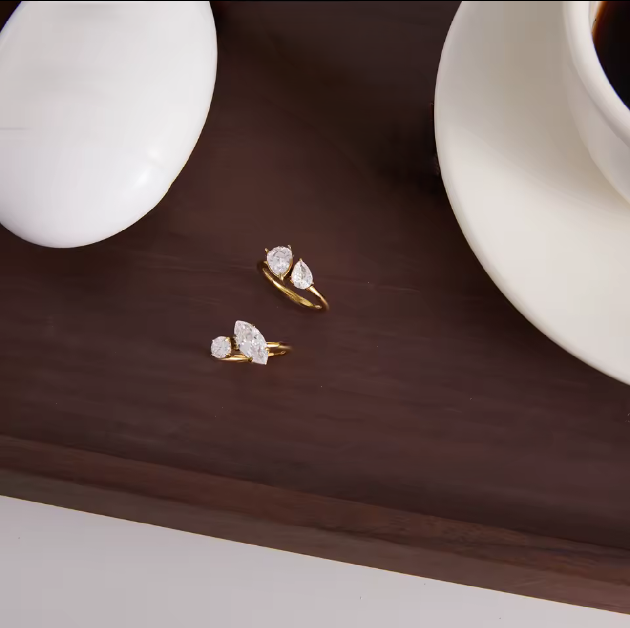 two gold rings with gemstones pictured on a dark mahogany table