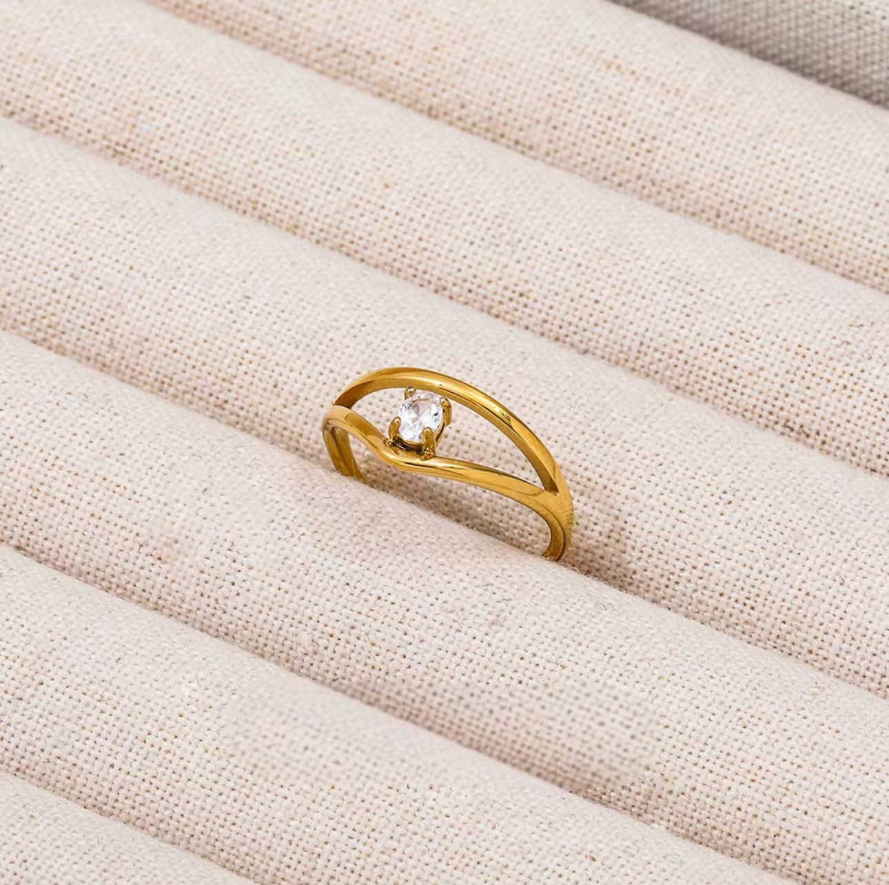 Gold ring with a diamond on a beige fabric surface