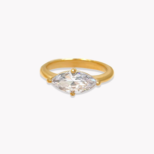 Gold ring featuring a large marquise shaped clear gemstone on a light grey background