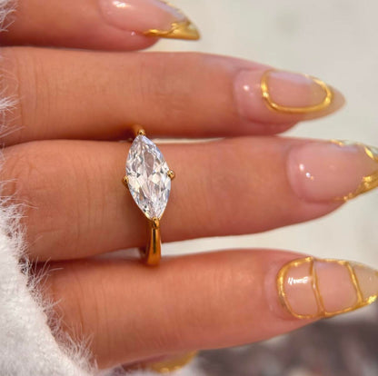 Gold ring featuring a large marquise shaped clear gemstone on a finger with manicured nails