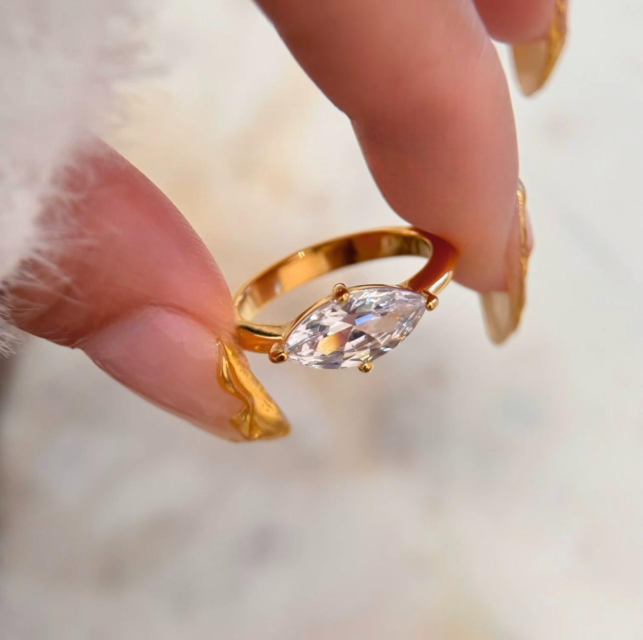 Gold ring featuring a large marquise shaped clear gemstone being held between two fingers