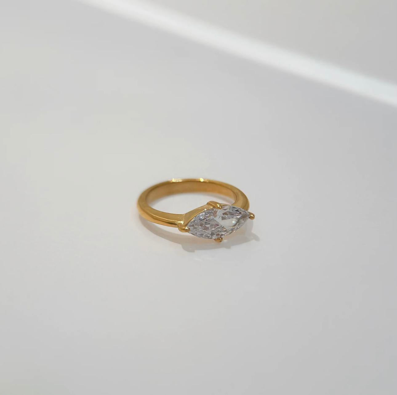 Gold ring featuring a large marquise shaped clear gemstone on a light grey background
