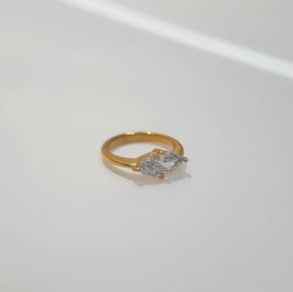Gold ring featuring a large marquise shaped clear gemstone on a light grey background