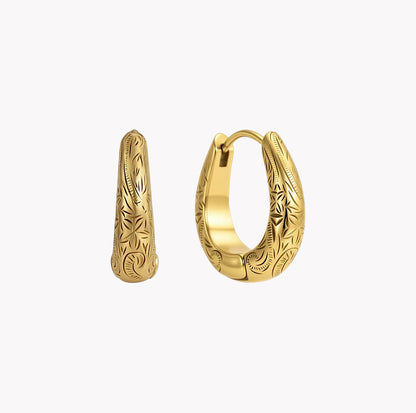 A pair of gold huggie hoop earrings with detailed floral engraving, shown on a light gray background.