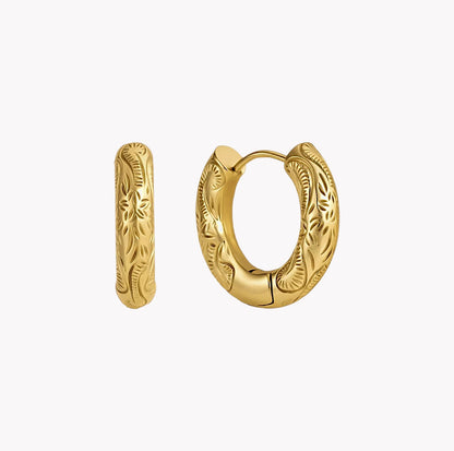 A pair of gold huggie hoop earrings with detailed floral engraving, shown on a clean white background.