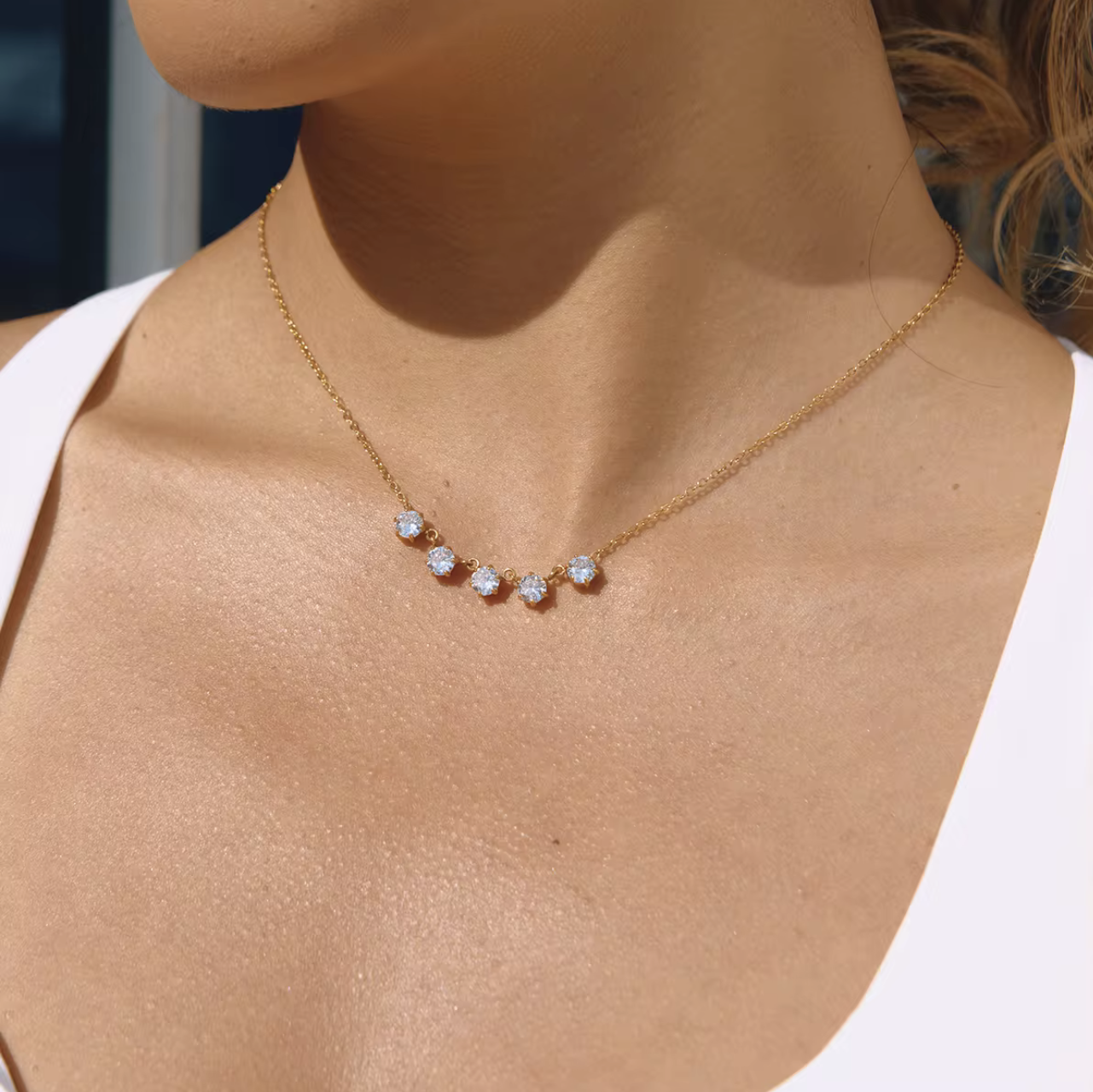 Gold necklace with small diamonds on a person wearing a white top.