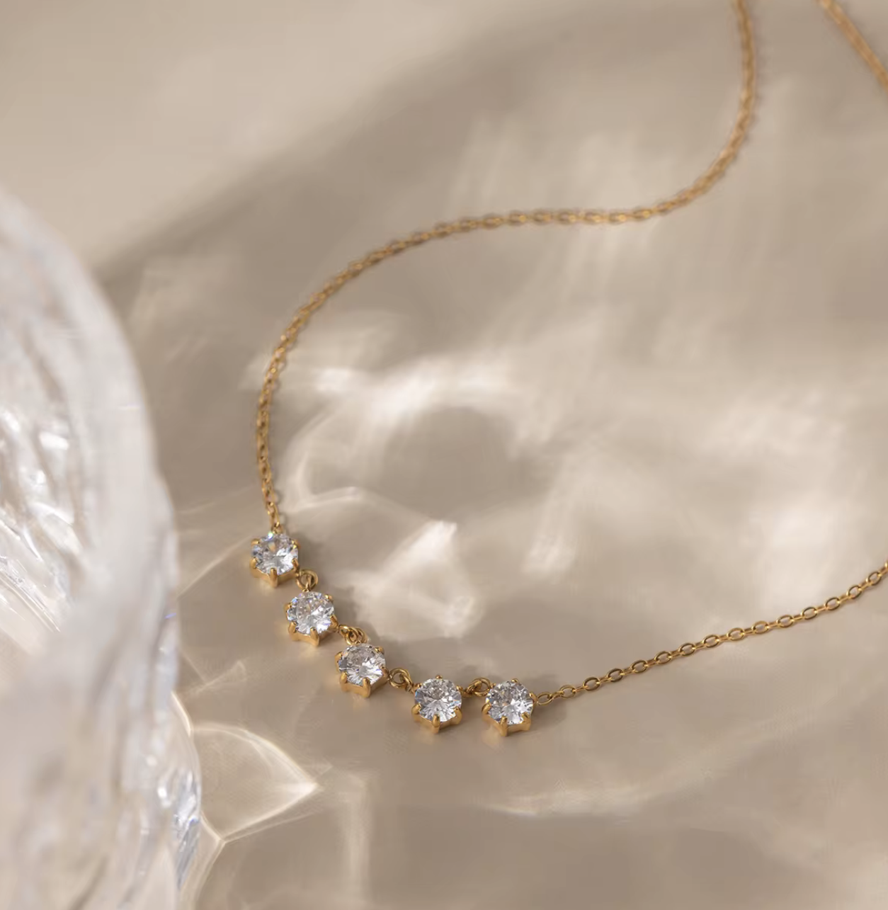 Gold necklace with diamond-like stones on a soft beige background