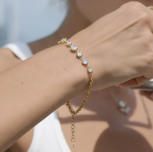 Gold bracelet with clear stones on a wrist against a neutral background