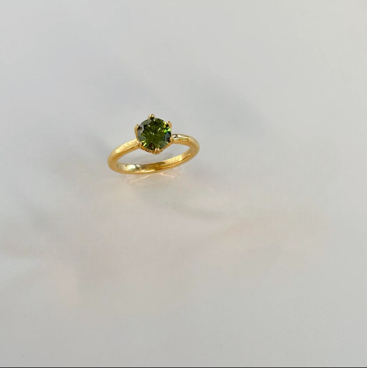 Gold ring with a green gemstone on a light grey background